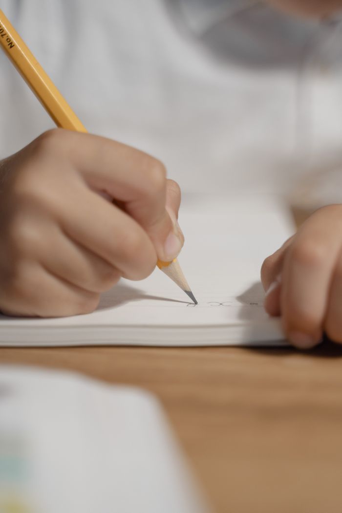 Close-up of a child's hand writing in a notebook with a pencil, focused on education